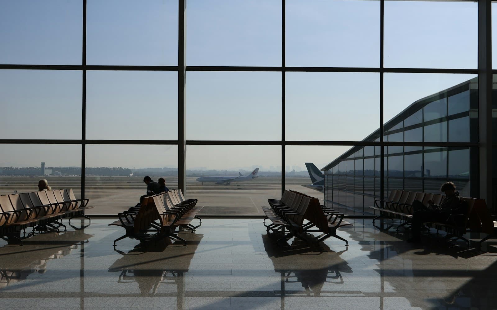 Passengers waiting beside large windows in an international airport terminal